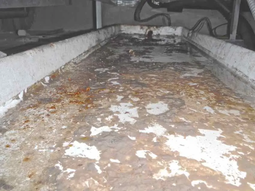 A drainage tray holding standing water, with rust staining and pale residue