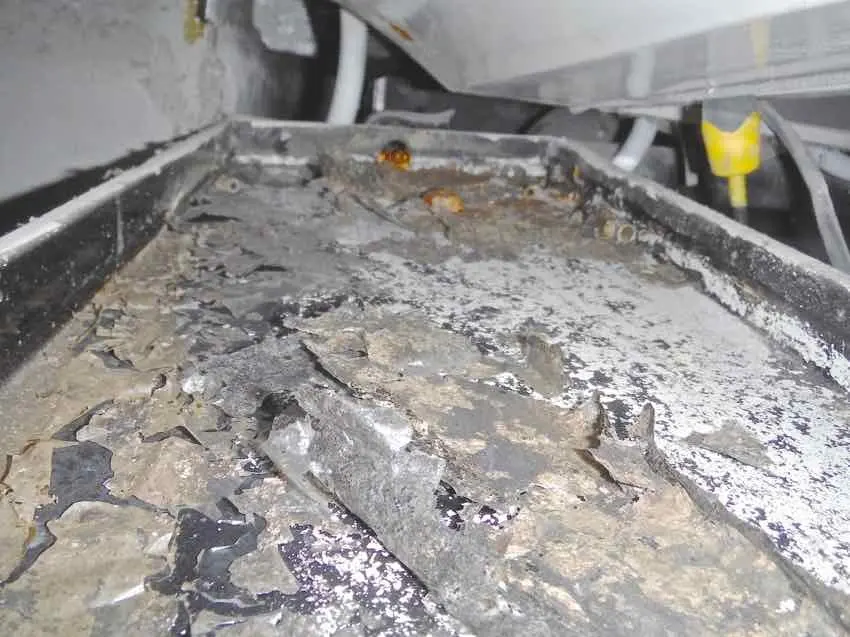 A drainage tray with its lining broken up and lifting away from the metal
