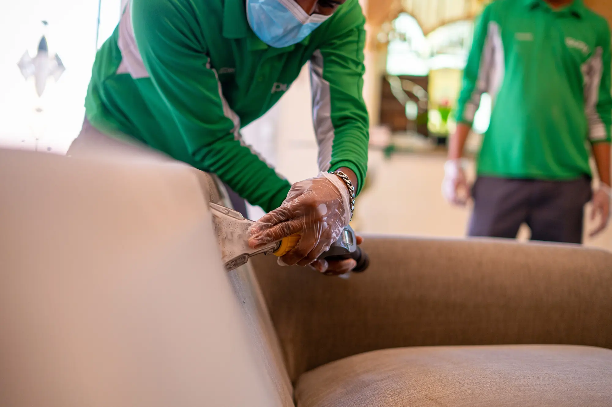 Two iPurity technicians in uniform and masks working along the arm of a sofa