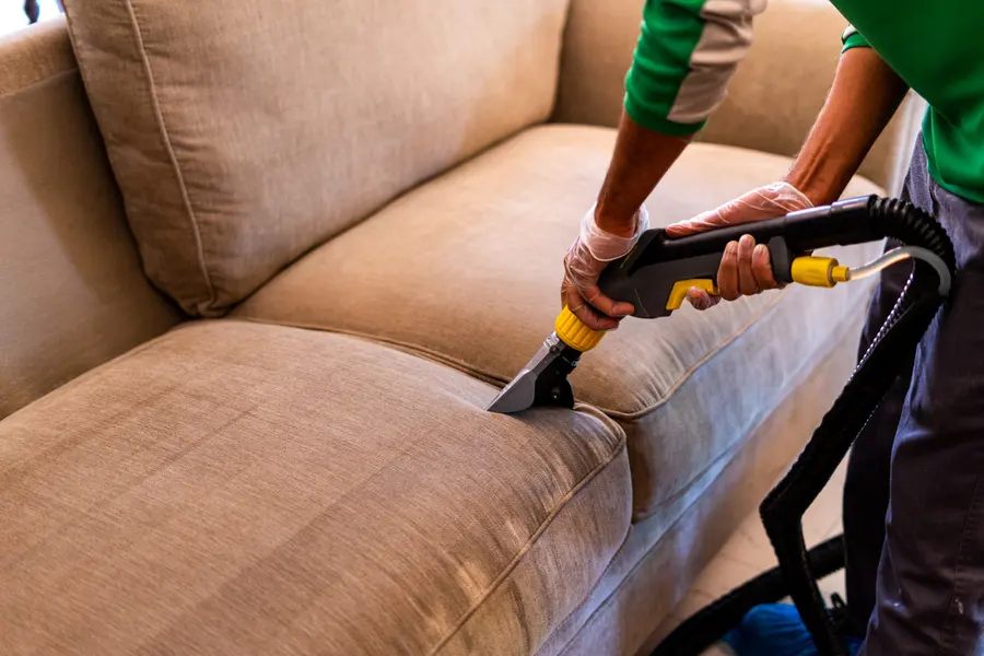 A technician drawing an extraction tool across a beige sofa cushion