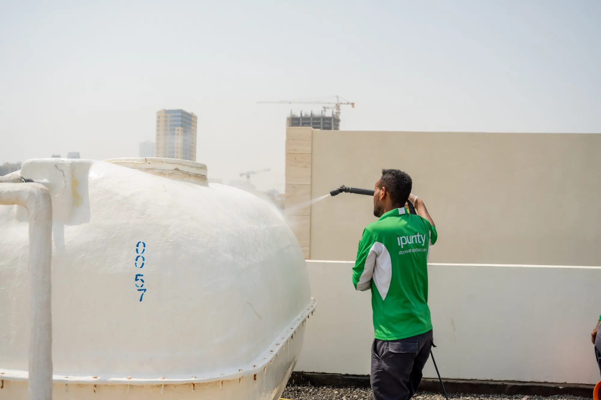 iPurity technician pressure-washing a rooftop water tank with the Dubai skyline behind