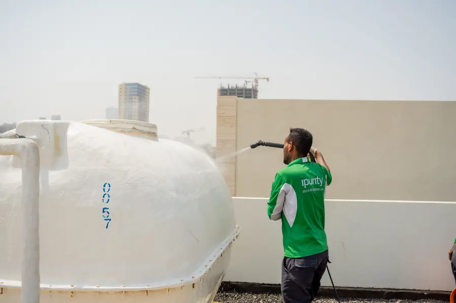 iPurity technician pressure-washing a rooftop water tank with the Dubai skyline behind