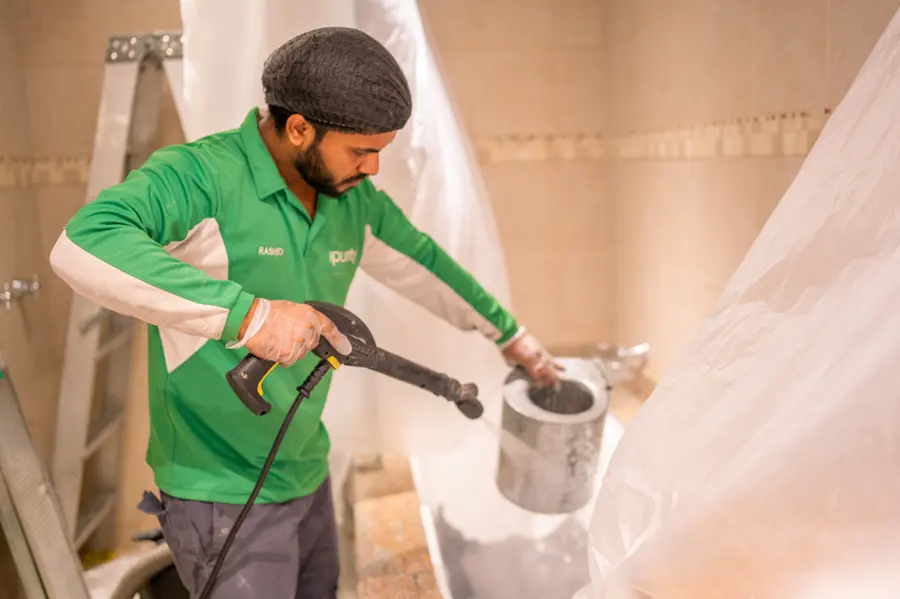 An iPurity technician rinsing a removed component with a pressure washer, protective sheeting behind