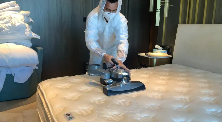 An iPurity technician in a protective suit and mask treating a mattress with a handheld machine