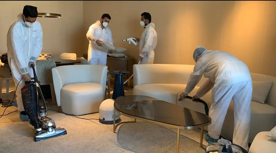 Four iPurity technicians in protective suits fogging a living room, one spraying while a fogging machine runs on the floor