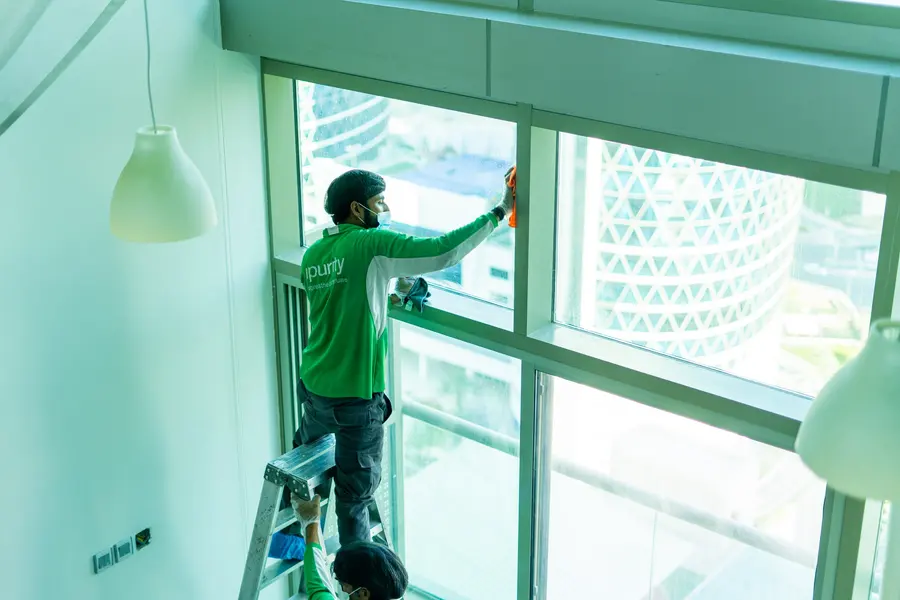 An iPurity technician on a stepladder cleaning the upper panes of a tall window